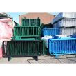 Close-up of black and green barriers, neatly stacked beside blue and white ones under bright sunlight.