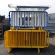 Stacked crowd control barriers in vibrant blue and yellow powder-coated finishes, arranged vertically in an outdoor industrial storage area.