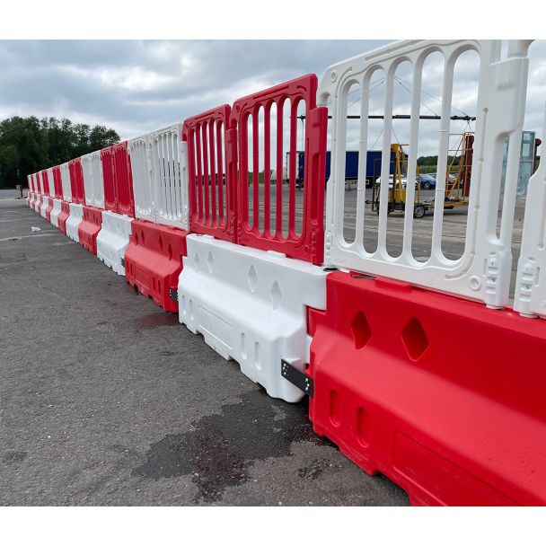 Long line of crash-tested Defender50 barriers with interlocking red and white plastic fencing, ideal for road safety and event management.