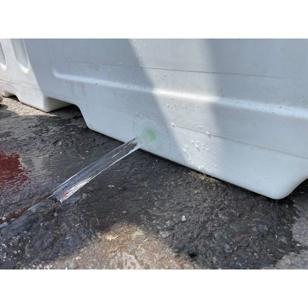 Water flowing from the drainage port of a white Defender50 barrier, demonstrating how barriers can be emptied after deployment.