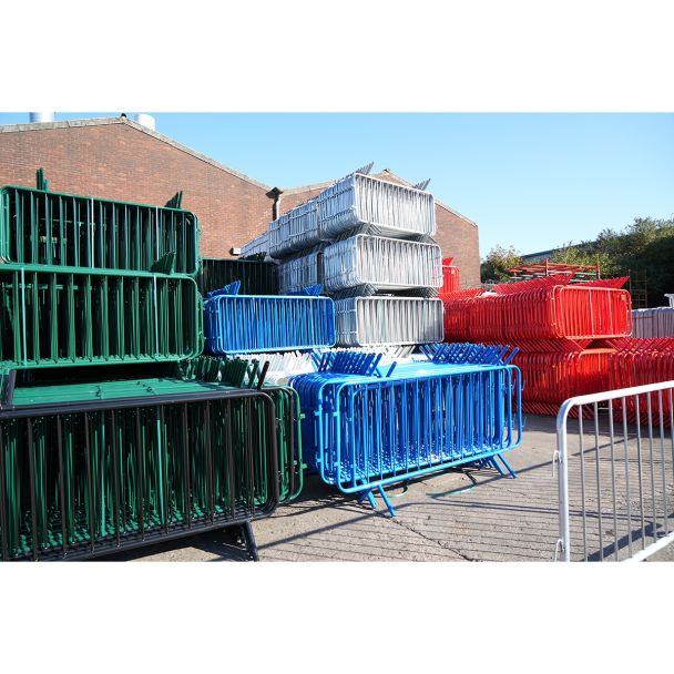 Stacked barriers in multiple colours (green, white, red, blue & black) organised outdoors near a brick building.
