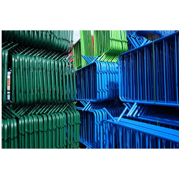 Tightly stacked green and blue barriers, with visible diagonal support legs in storage yard.