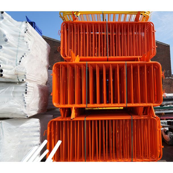 Vivid orange powder-coated steel crowd barriers stacked vertically in a warehouse yard.
