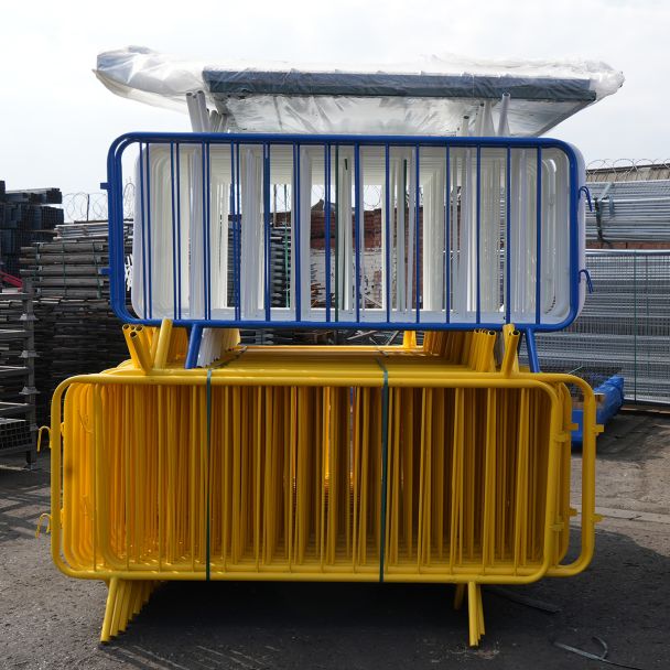 Stacked yellow and blue powder-coated crowd control barriers with fixed legs, neatly arranged outdoors in a storage yard.