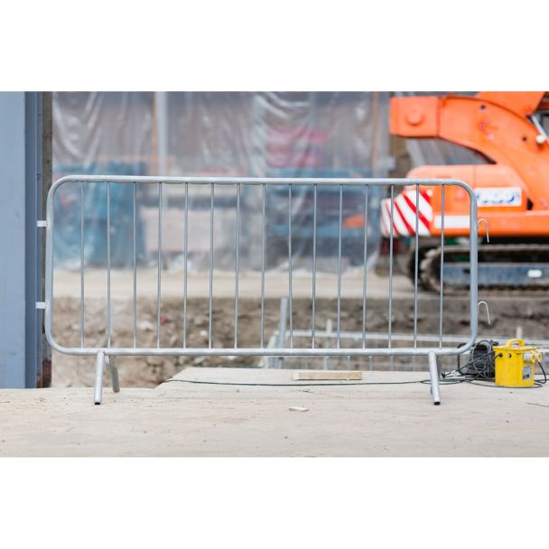 Galvanised crowd control barrier placed on a construction site with a digger in the background.