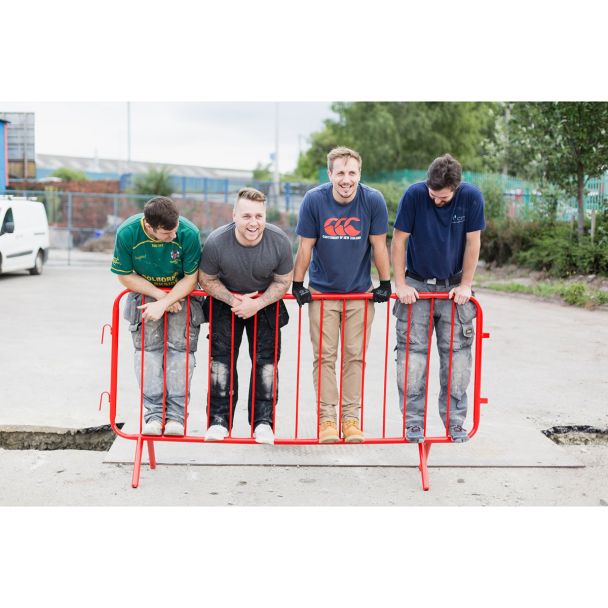 Four workers standing on a red crowd control barrier, showcasing its durability and load-bearing capacity in a practical test.